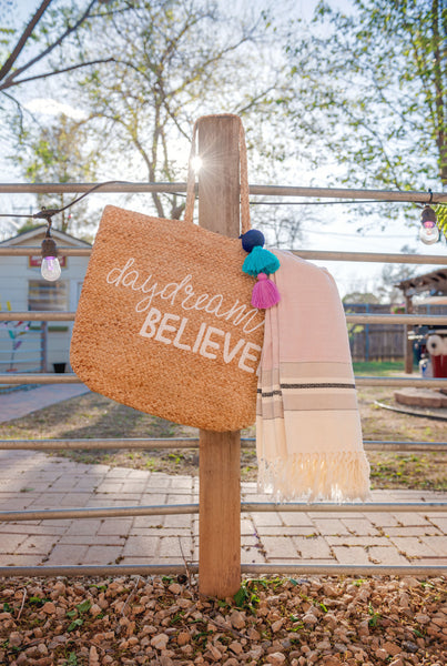Daydream believer jute beach bag with throw bundle hanging on a fence. 