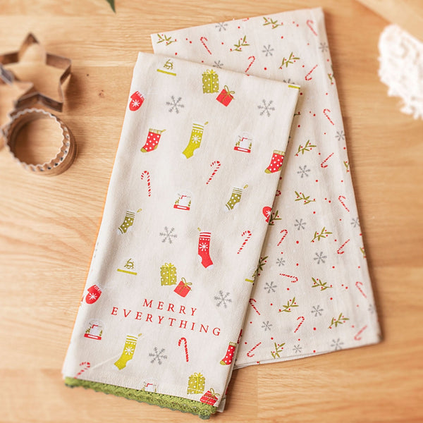 Merry Everything holiday flour sack tea towel with charm on a table with cookie cutters. 