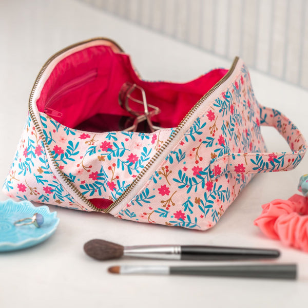Blush floral zip cosmetic bag on a table with cosmetic tools