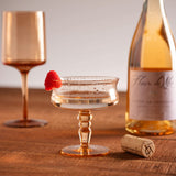 Heirloom rose vintage coupe glass on a table with a bottle of wine and a cork.