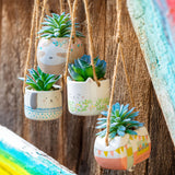 Shaped hanging succulent pots hanging in front of a fence.