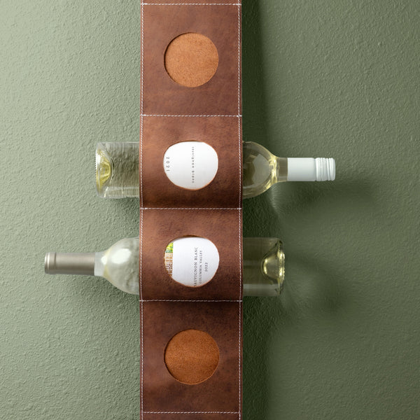Leather hanging wine holder with two wine bottles in front of a green wall