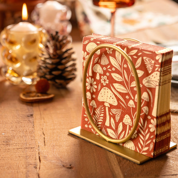 Mushroom cocktail paper napkins in gold napkin holder on a table.